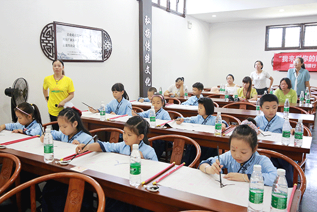 学老师为萌娃们讲解毛笔握笔和书写的方法，随后，萌娃们在志愿者的指导下学写“人”字。.gif